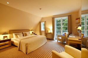 A hotel room with a large bed, a desk with a chair, and a window with curtains.