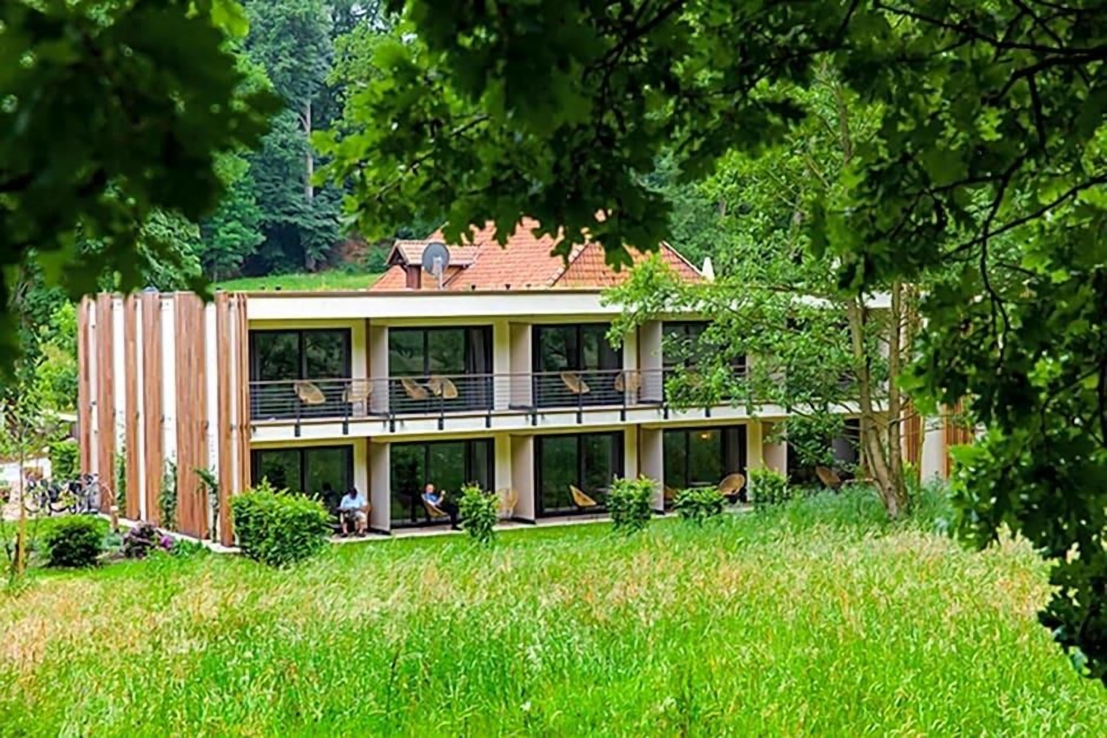 A two-story building with a balcony on the upper floor, surrounded by greenery.