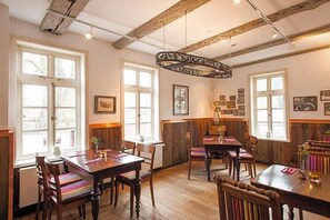A dining area with wooden tables and chairs, large windows, and a rustic ceiling.