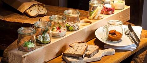 A wooden table with various food items and utensils, including bread, jars of pickles, and a plate with a fork and knife.