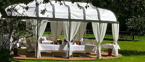 A tent with white drapes, round tables, and chairs arranged inside.