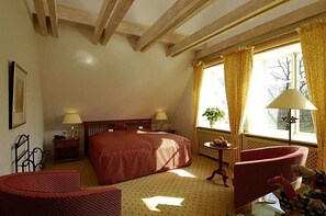 A hotel room with a large bed, two bedside tables, a chair, a small table with a lamp, and a window with curtains.