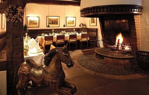 A dining area with a fireplace, a horse sculpture, and framed pictures on the wall.