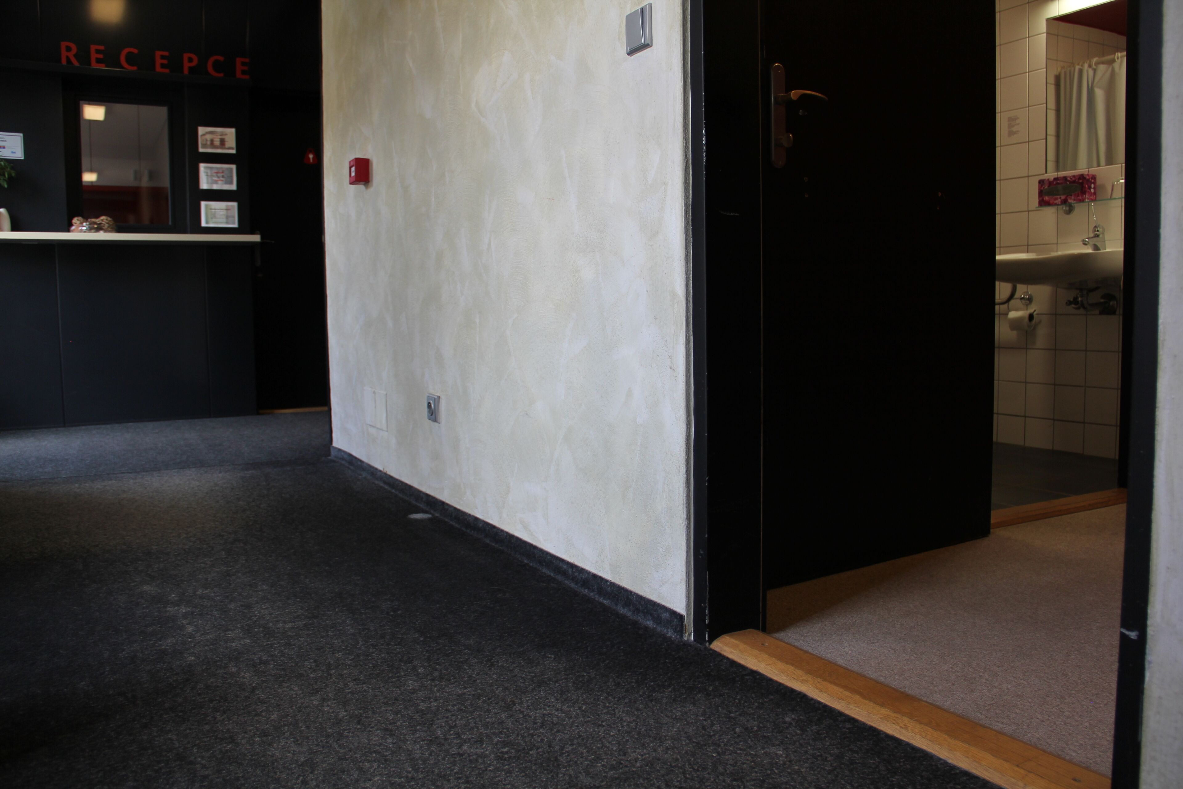 Un couloir avec un comptoir d’accueil portant l’inscription « RÉCEPTION » et des toilettes visibles à travers une porte ouverte.