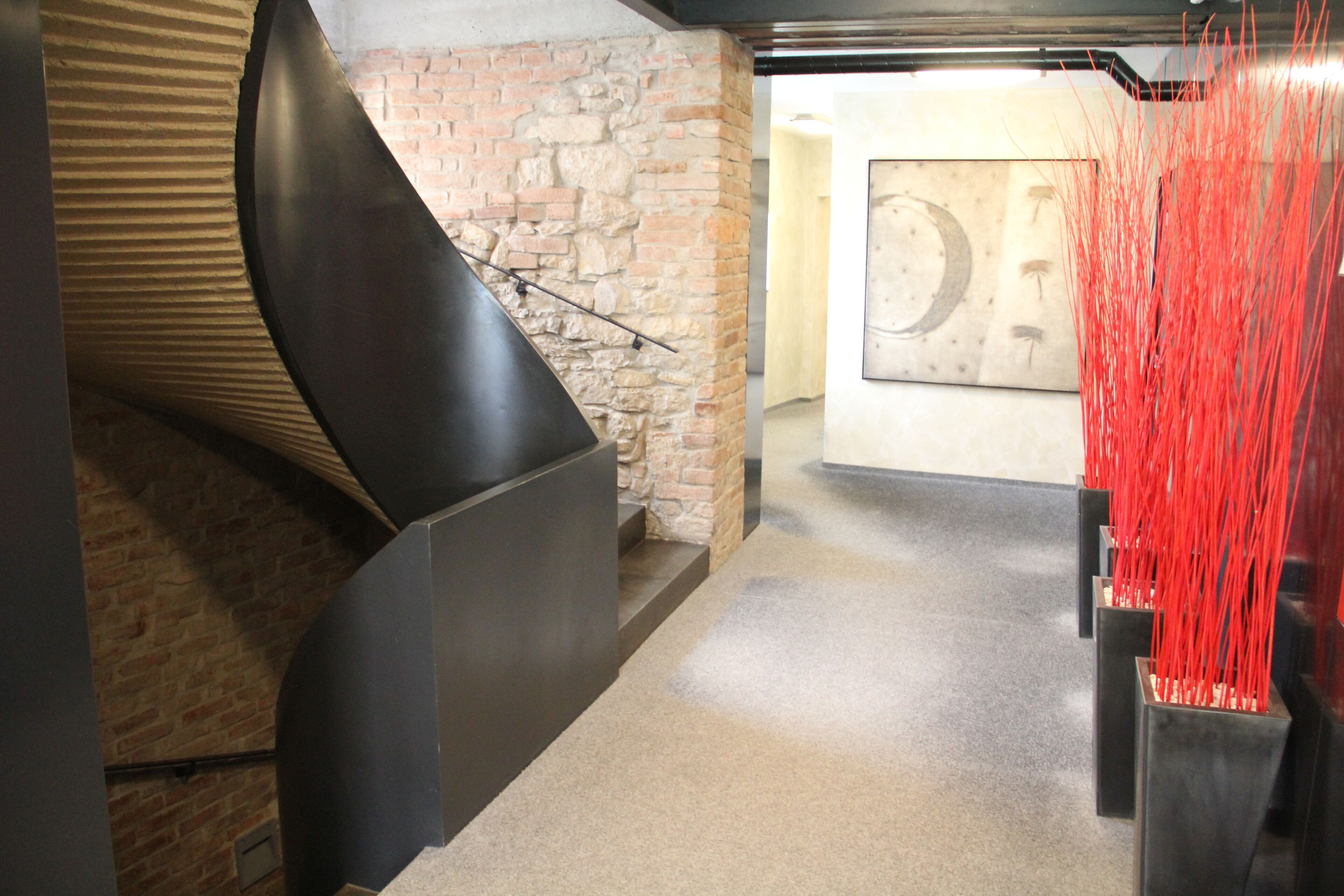A modern interior with a curved black structure, a stone wall, and red vertical elements.
