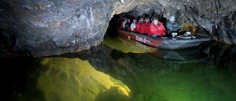 A group of people in a boat inside a cave with a rocky ceiling and greenish water.