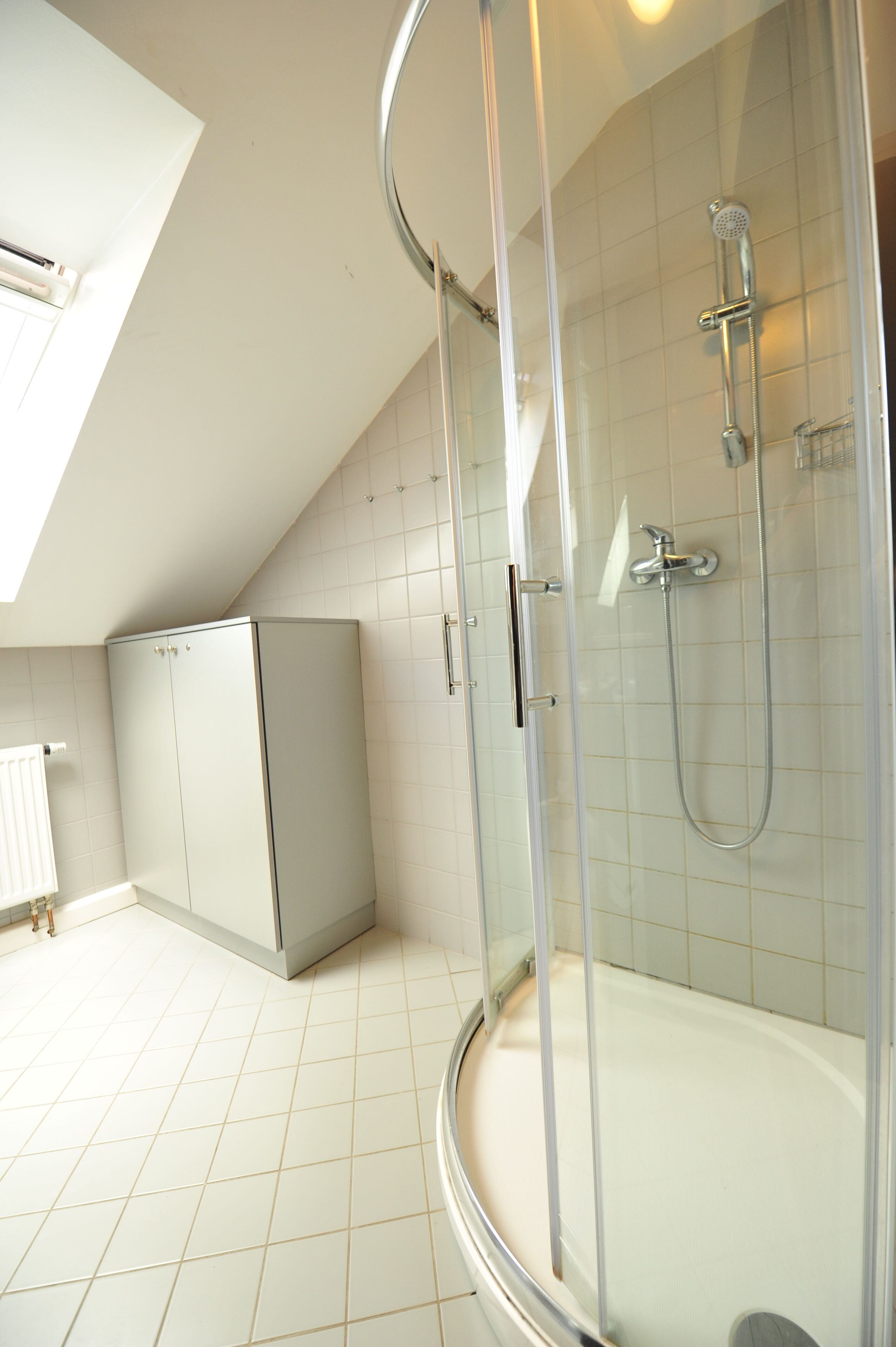 A modern bathroom with a glass-enclosed shower, a white bathtub, and a built-in cabinet.