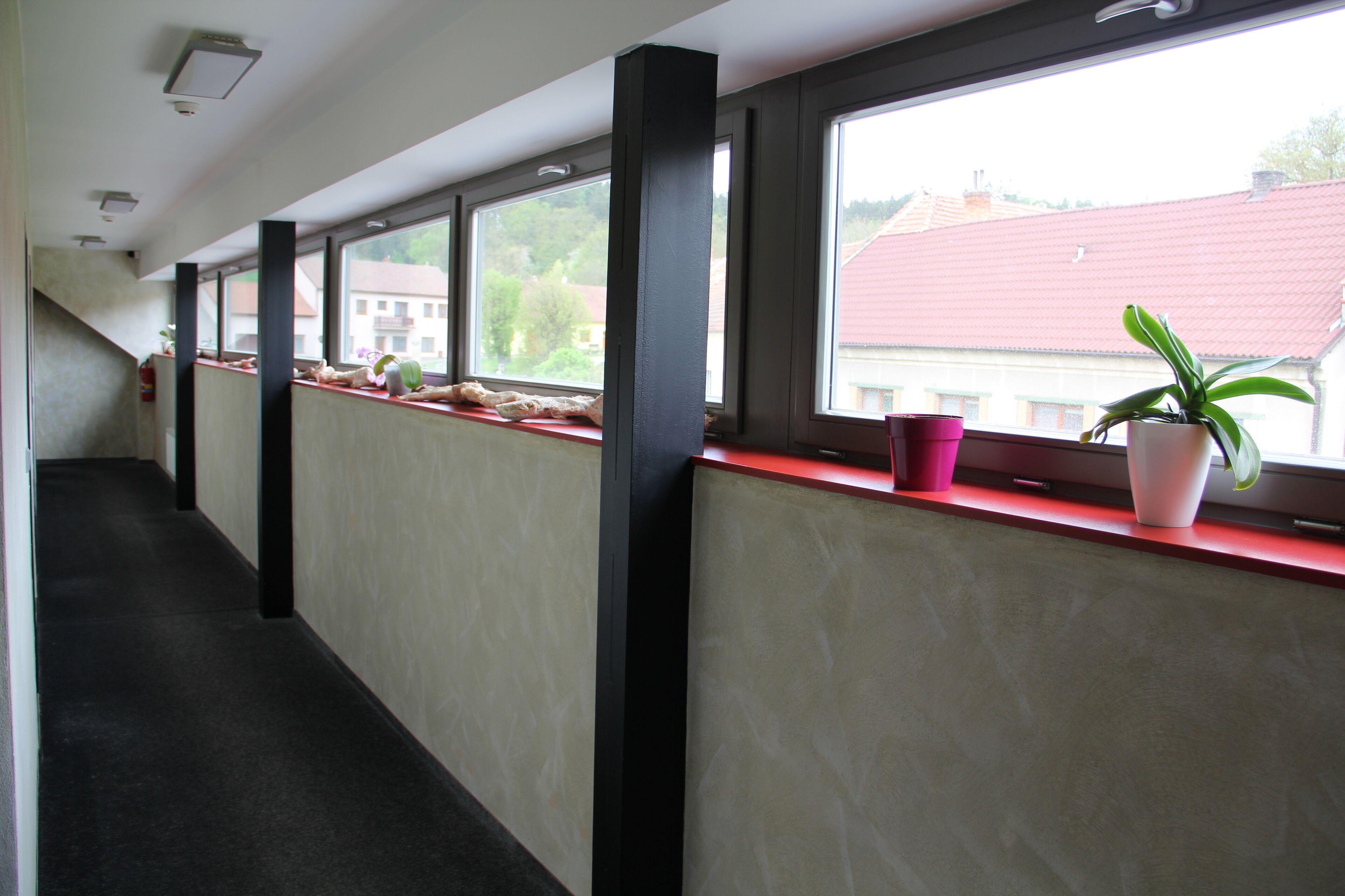 Un pasillo con ventanas, un alféizar rojo y una planta en maceta.