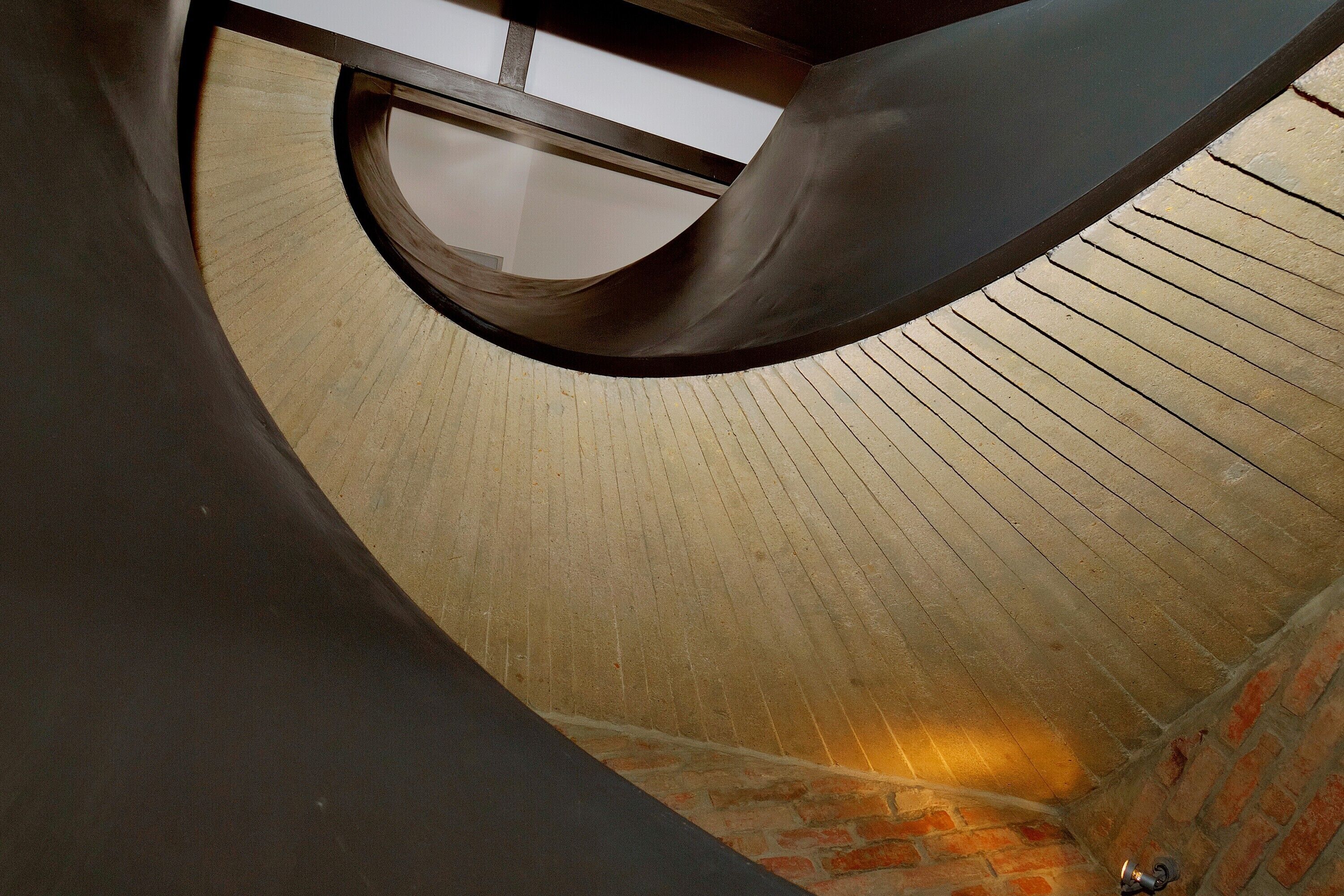 Elemento arquitetônico curvo com piso de madeira e parede de tijolos.