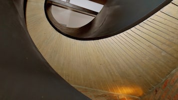 Elemento arquitetônico curvo com piso de madeira e parede de tijolos.