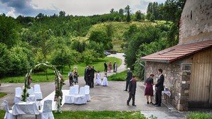 An outdoor wedding venue with white tables and chairs, a stone building, and a lush green landscape. - Hotel U Tri volu (Býkovice)