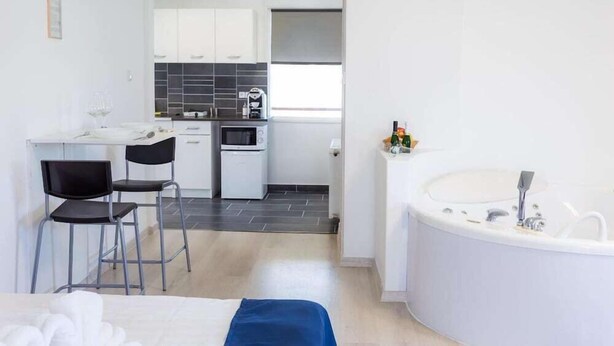 A compact hotel room with a bed, a small kitchenette, a sitting area with chairs, and a bathroom with a bathtub. - Classic (Budapest)
