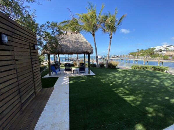 A wooden deck with a thatched-roof gazebo, two chairs, and a small table.