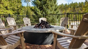 Una terraza con sillas Adirondack, una mesa redonda y un pozo de fuego.