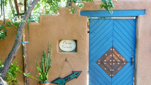 A blue door with a diamond pattern, a sign reading "Casa Verde," and a decorative arrow on a beige wall.