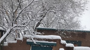 A snow-covered building with a blue door, a small stool, and two signs indicating 'Casa Verde' and 'Casa Azul'.
