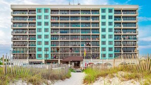 A multi-story hotel with a central entrance, balconies on each floor, and a sandy beach area in front. - Beautiful direct Gulf view & beach front condo. (Gulf Shores)