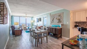 A spacious living area with a dining table, chairs, and a kitchen area with cabinets and a countertop. - Beautiful direct Gulf view & beach front condo. (Gulf Shores)