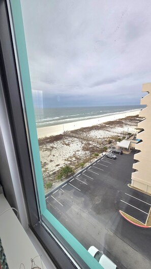 Une vue sur une plage, prise depuis une fenêtre, qui inclut un parking et un bâtiment doté d’une architecture originale.