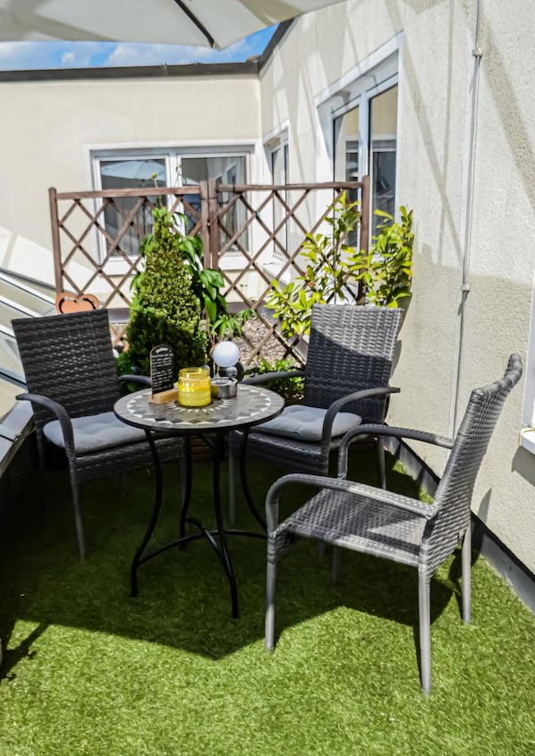 An outdoor seating area with a round table and four chairs, surrounded by a white wall and a wooden fence. - Grunau (Bayreuth)