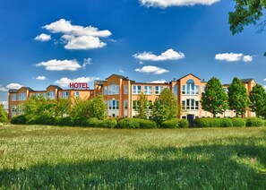 A hotel with multiple buildings, a clear sky, and a grassy field in front.