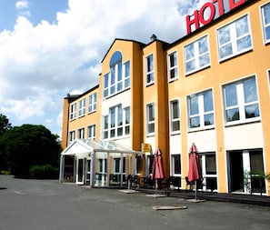 A hotel with a yellow facade, multiple windows, and a covered entrance area with outdoor seating.