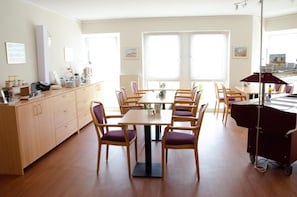 A dining area with a long table, multiple chairs, and a kitchen area with cabinets and appliances.