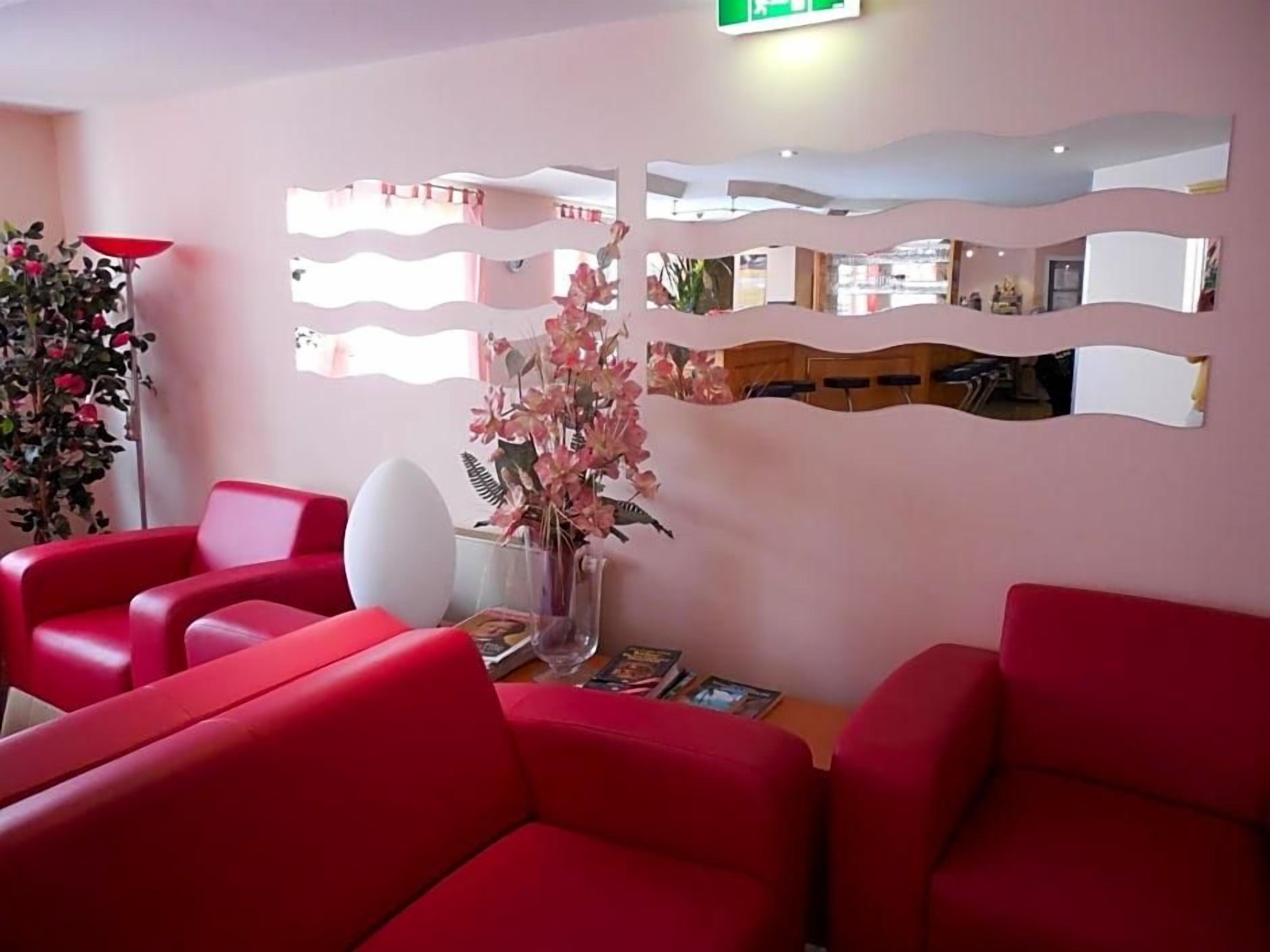 Ein Empfangsbereich mit roten Sitzgelegenheiten, einer Vase mit rosa Blumen und einer Wand mit dekorativen Spiegeln.