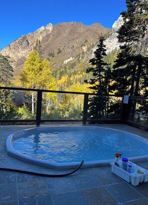 A hot tub with a mountain view, surrounded by trees and a wooden deck.