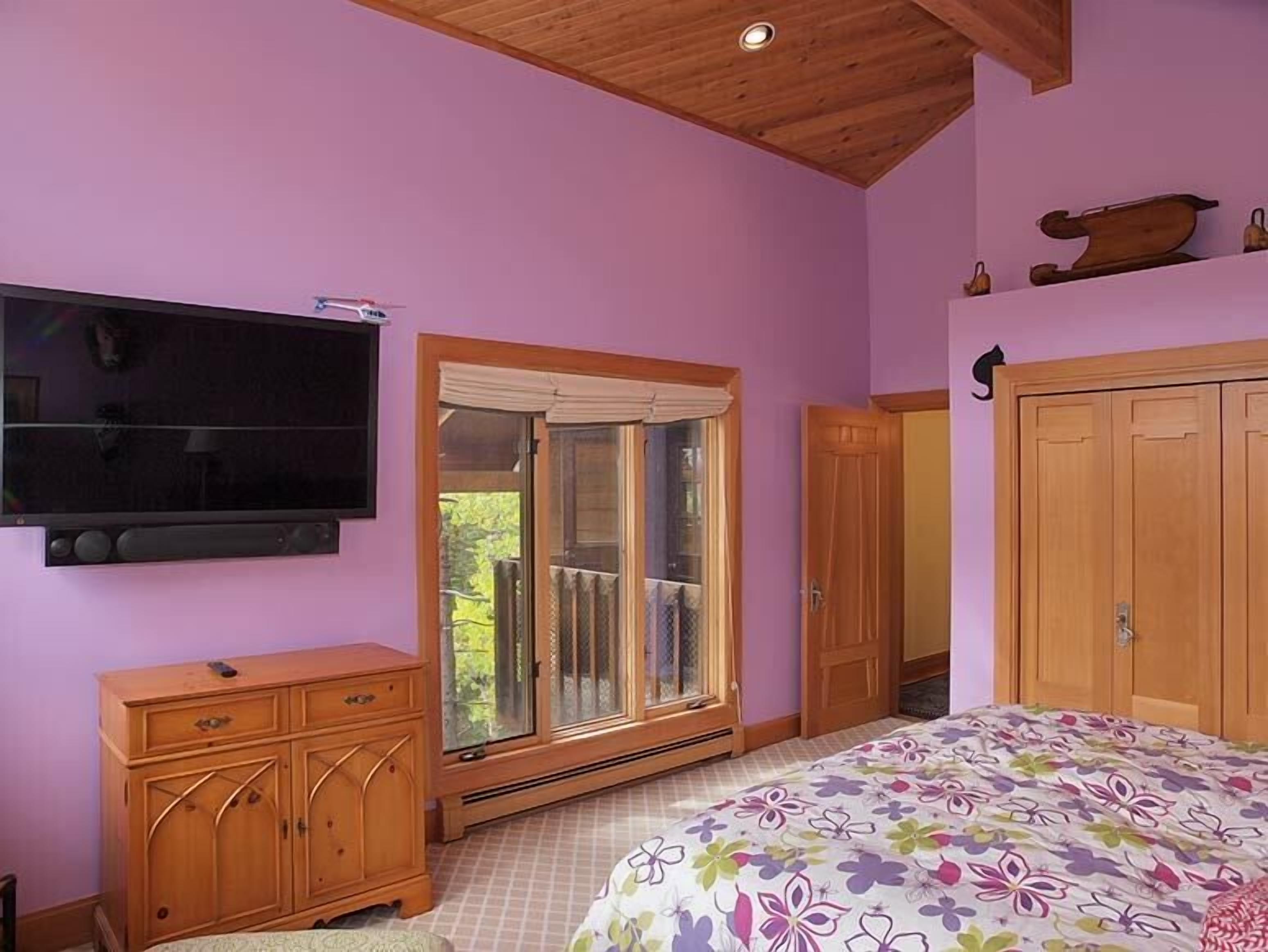 Une chambre dotée d’un grand lit, d’un téléviseur fixé au mur, d’une armoire en bois et d’une fenêtre donnant sur un paysage verdoyant.