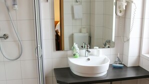 Ein Badezimmer mit einer Duschkabine, einem weißen Waschbecken mit schwarzer Arbeitsplatte, einem Spiegel über dem Waschbecken und einer Toilette.