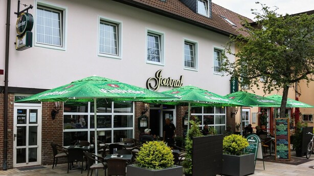 Ein Restaurant mit Außenbereich, einem Schild mit der Aufschrift 'Journal' und einem Schild 'Zimmer 1-10', das freie Zimmer andeutet.