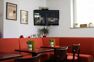 Una habitación con un sofá rojo, dos mesas con sillas, un televisor montado en la pared y una ventana con vista a la ciudad.