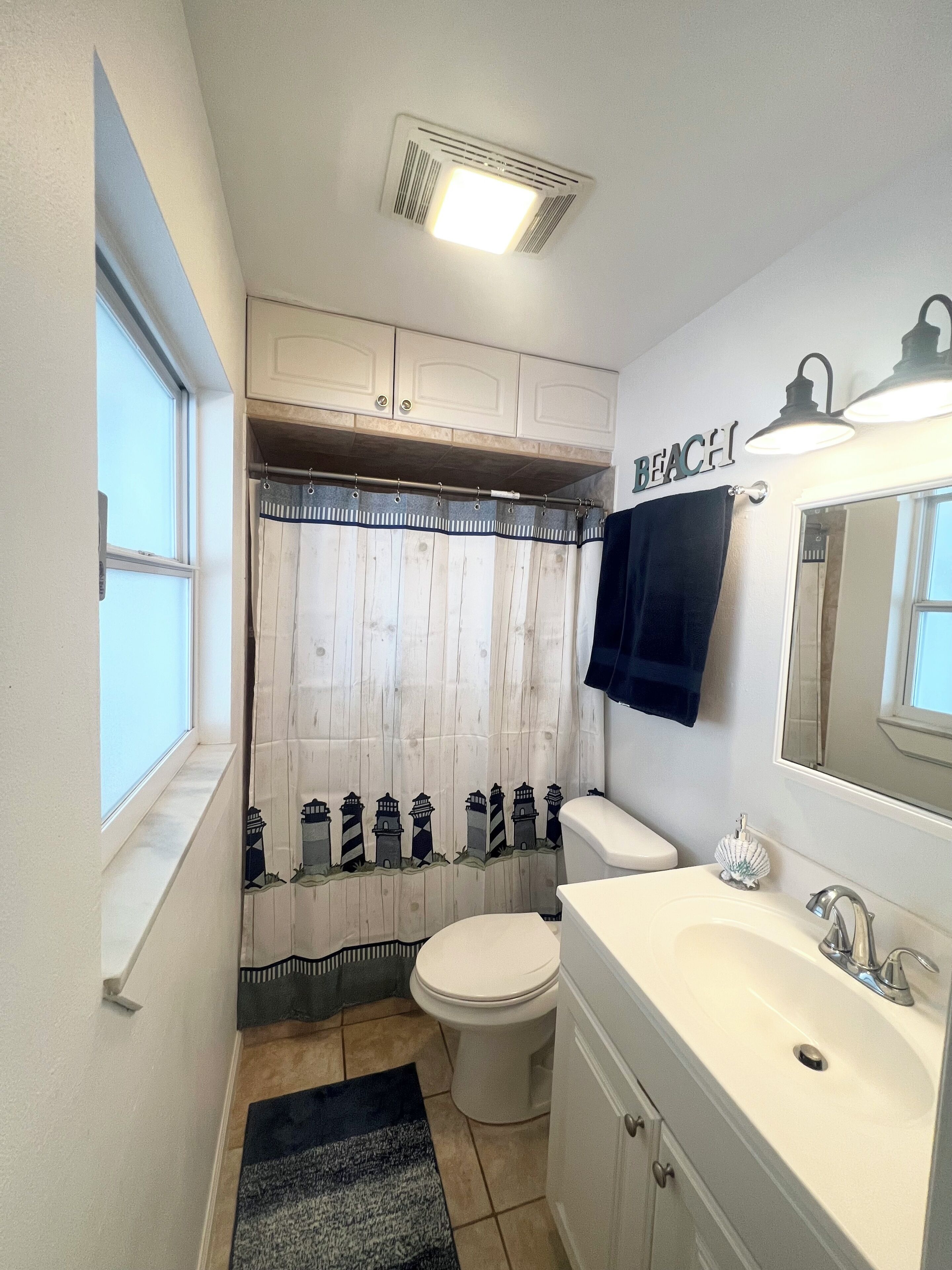 A bathroom with a toilet, sink, and shower curtain with lighthouse designs.