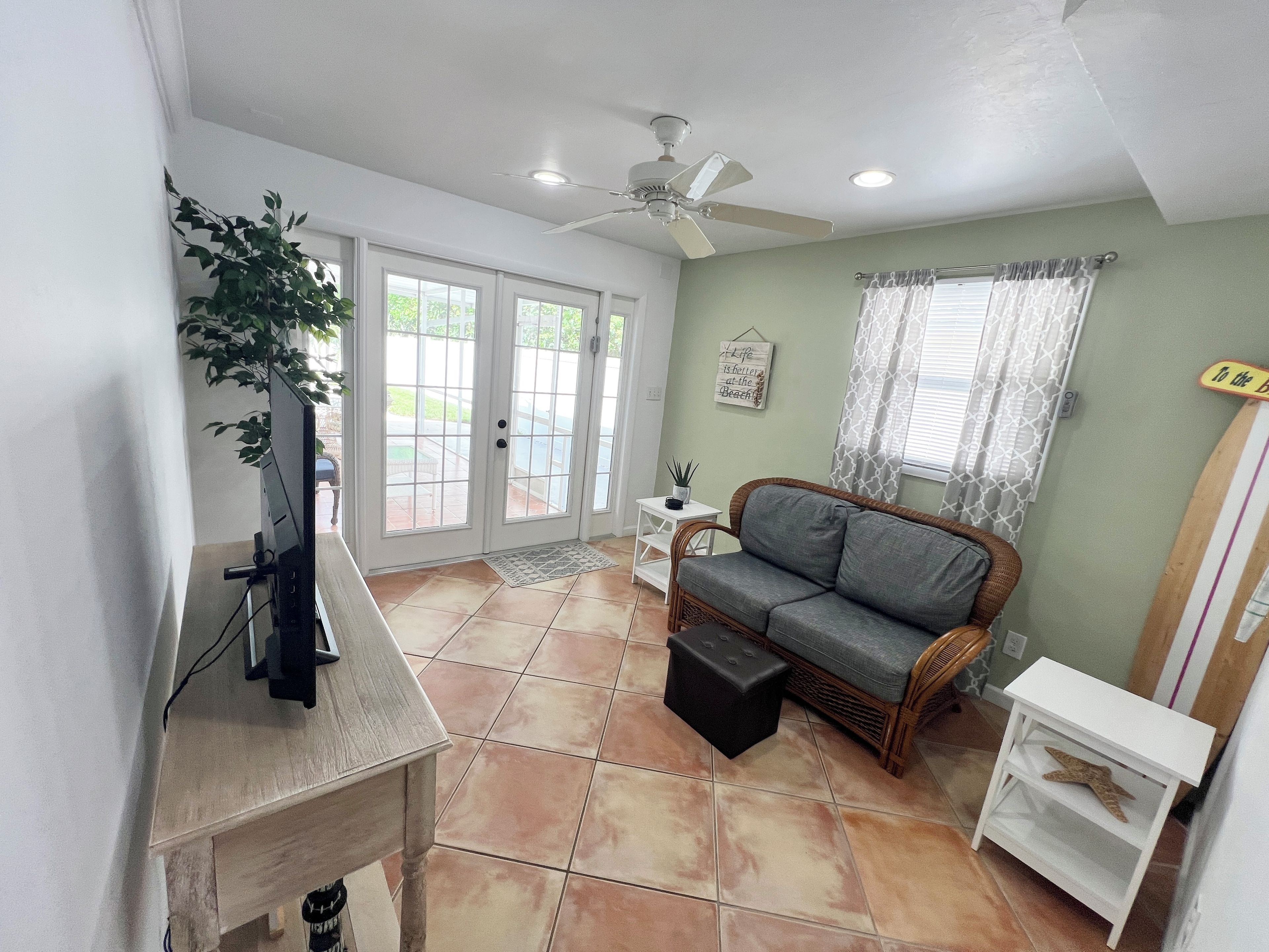 A living room with a television, a ceiling fan, a sofa, a small table, and a window with curtains.