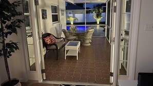 En öppen uteplats med en pool, utemöbler och utsikt över trädgården.