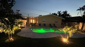 En trädgård med en pool, ett hus och palmer runt omkring.