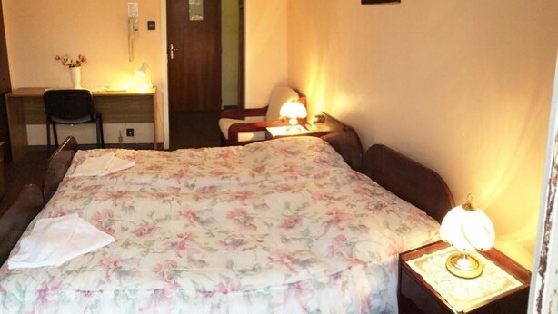Una habitación de hotel con una cama, dos mesitas de noche, un escritorio, una silla y una puerta.