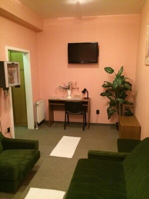 A small living room with a green sofa, a wooden table, a television, and a potted plant.