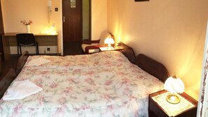 Una habitación de hotel con una cama, dos mesitas de noche, un escritorio, una silla y una puerta.