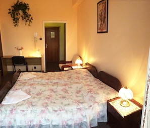 A hotel room with a bed, two bedside tables, a desk, a chair, and a door.