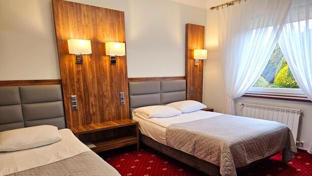 A hotel room with two beds, a wooden headboard, a red carpet, and a window with curtains. - Hotel Hawana (Bydgoszcz)