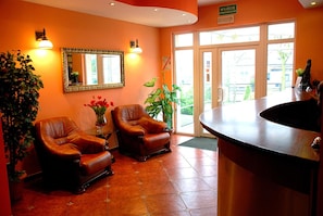 A reception area with two leather chairs, a mirror, a vase with flowers, and a reception desk.