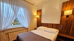 A hotel room with a bed, a window with sheer curtains, a wall-mounted lamp, and a radiator. - Hotel Hawana (Bydgoszcz)