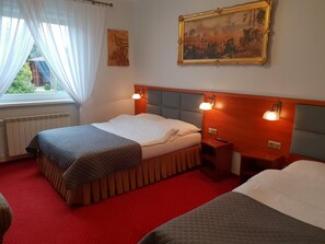 Ein Hotelzimmer mit Bett, Nachttisch, Lampe, einem Bild an der Wand und einem Fenster mit Vorhängen.