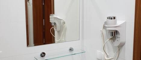 Casa de banho com lavatório branco, espelho, secador de cabelo e porta-toalhas.
