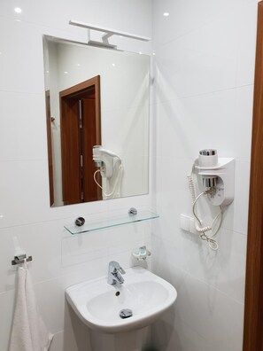 Casa de banho com lavatório branco, espelho, secador de cabelo e porta-toalhas.