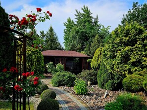 Um jardim com um gazebo, um caminho de pedra e diversas arbustos e árvores.
