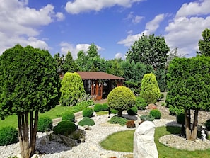 Um jardim bem cuidado, com um gazebo, sebes aparadas e diversas árvores.