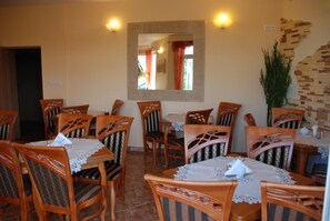 A dining area with wooden chairs and tables, a mirror on the wall, and a potted plant.
